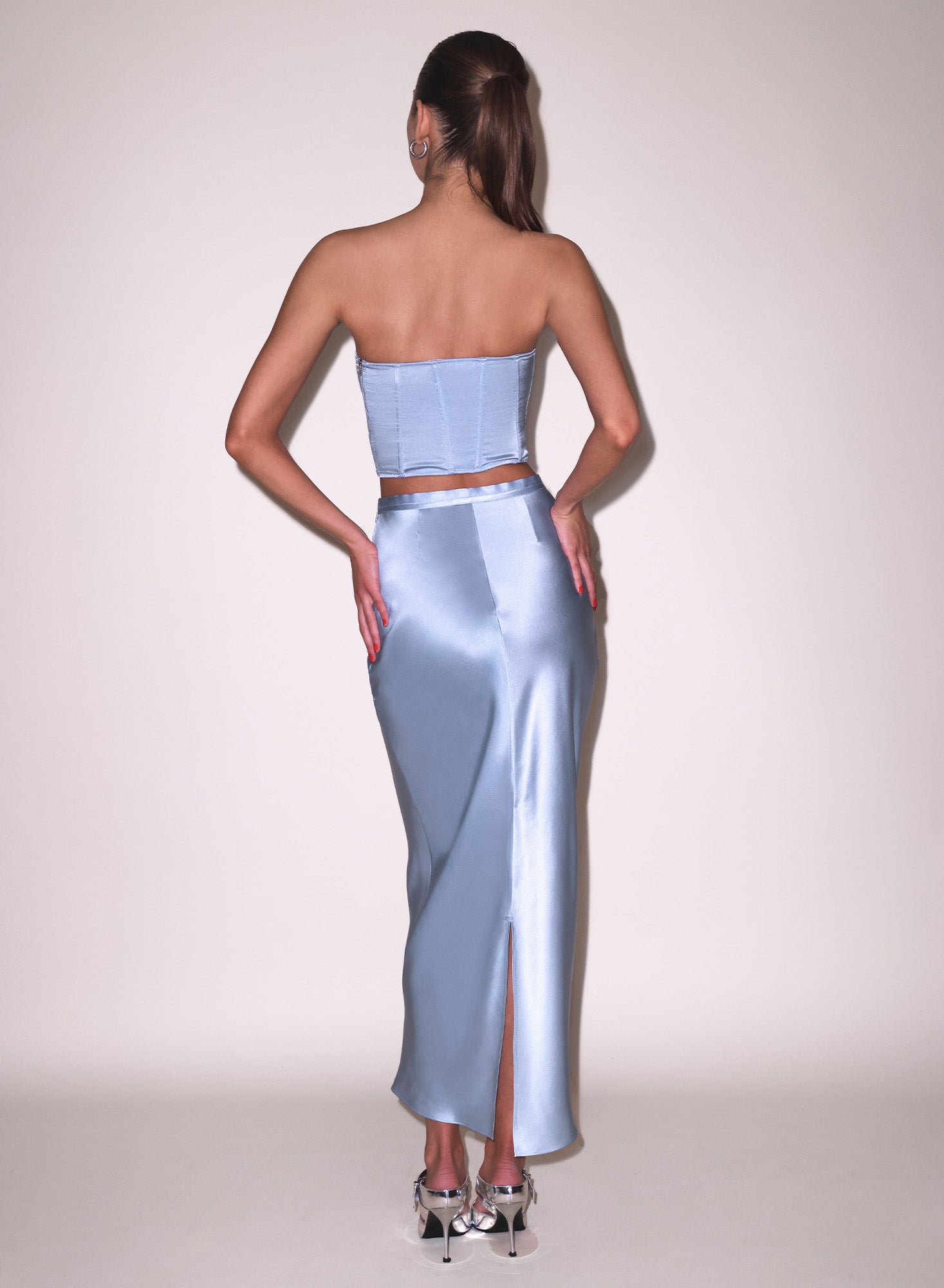 back view of model wearing a light blue satin strapless top and blue pencil skirt 